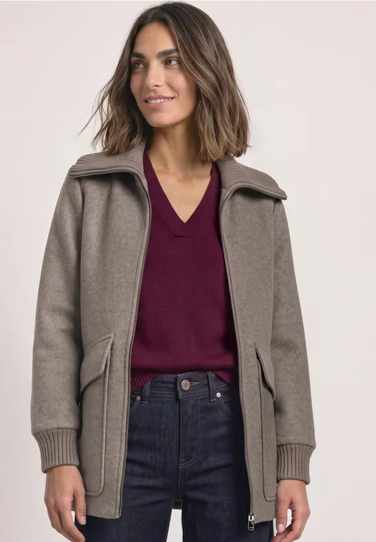 Frau in braunem Mantel, bordeauxrotem V-Ausschnitt-Pullover und Jeans