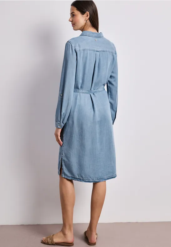 Frau von hinten in einem knielangen Jeanskleid mit langen Ärmeln, barfuß.