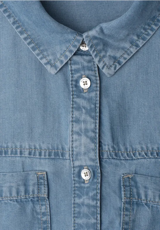 Nahaufnahme einer blauen Jeansjacke mit Metallknöpfen und aufgesetzten Brusttaschen.