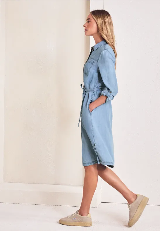 Seitliches Profil einer Frau in hellblauer Denim-Overall mit Gürtel und Plateau-Schuhen.