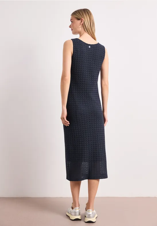 Frau von hinten in navy-blauem, ärmellosem Midikleid mit feinem Quadratmuster und weißen Sneakern.