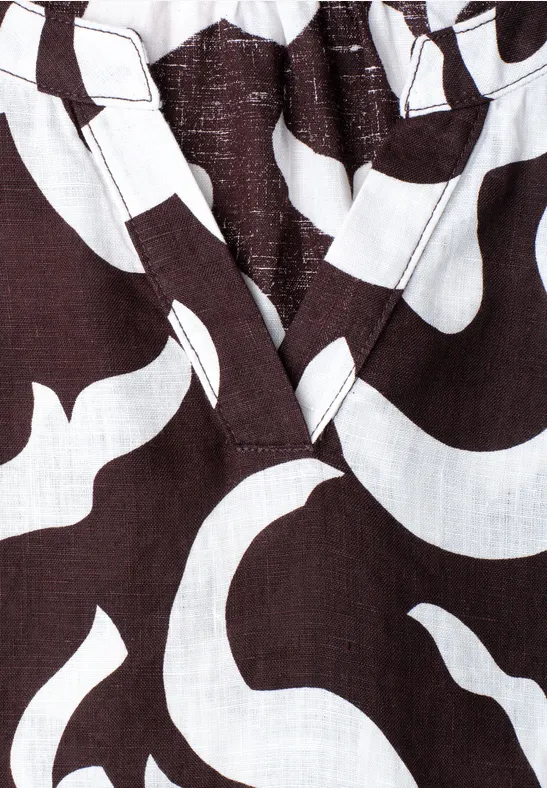 Nahaufnahme eines dunkelbraunen Stoffes mit weißen, geschwungenen Mustern und V-Ausschnitt.