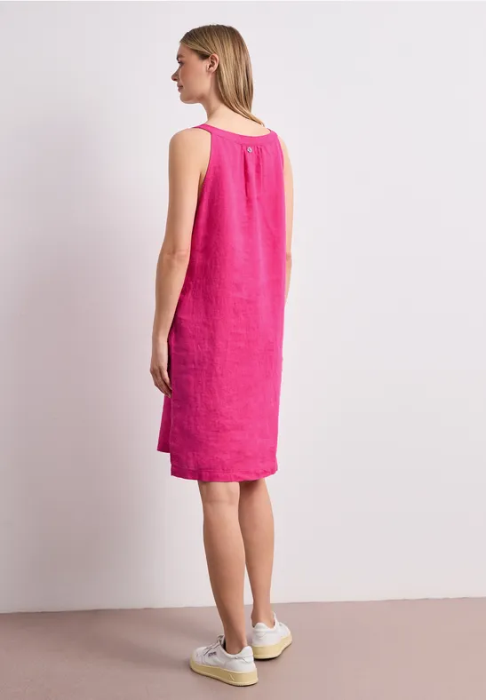 Frau seitlich stehend in einem knielangen, ärmellosen pinken Leinenkleid und weißen Sneakern