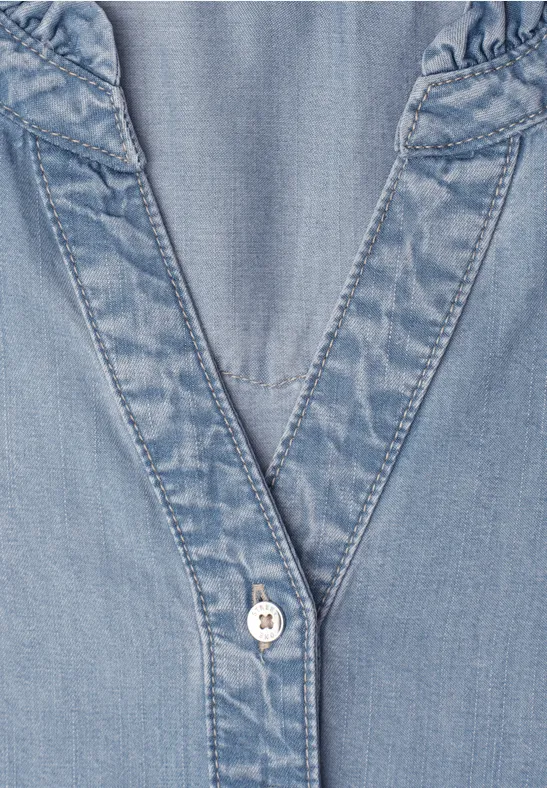 Close-up van een lichtblauw denim bovenstuk met V-hals en knoop