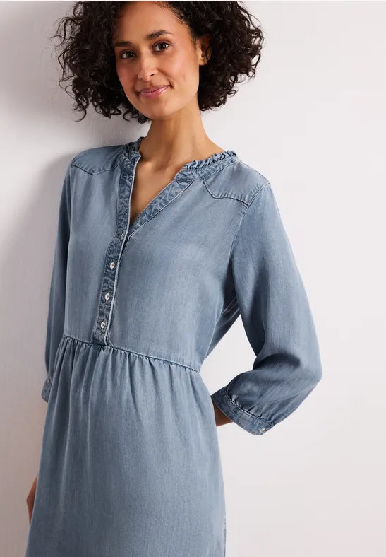 Vrouw in lichtblauwe spijkerjurk met knopen, elastische taille en lange mouwen.