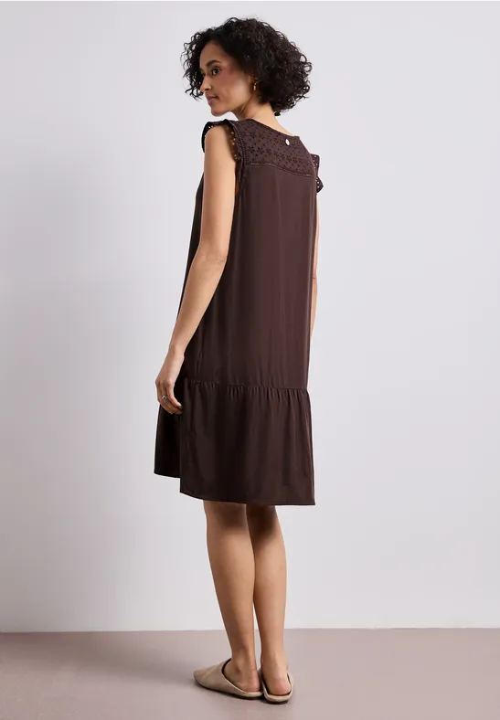 Femme vue de dos portant une robe marron sans manches à volants, dans un décor épuré, avec sandales.