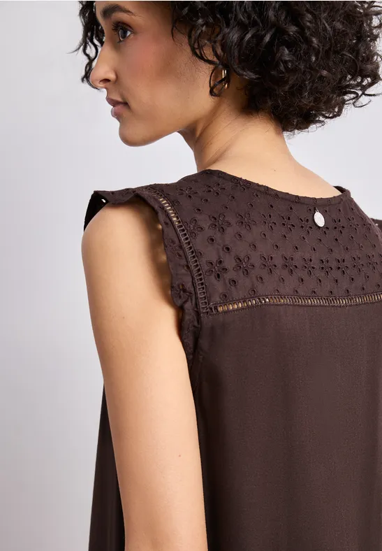 Femme de profil portant un top sans manches marron avec dentelle sur les épaules.