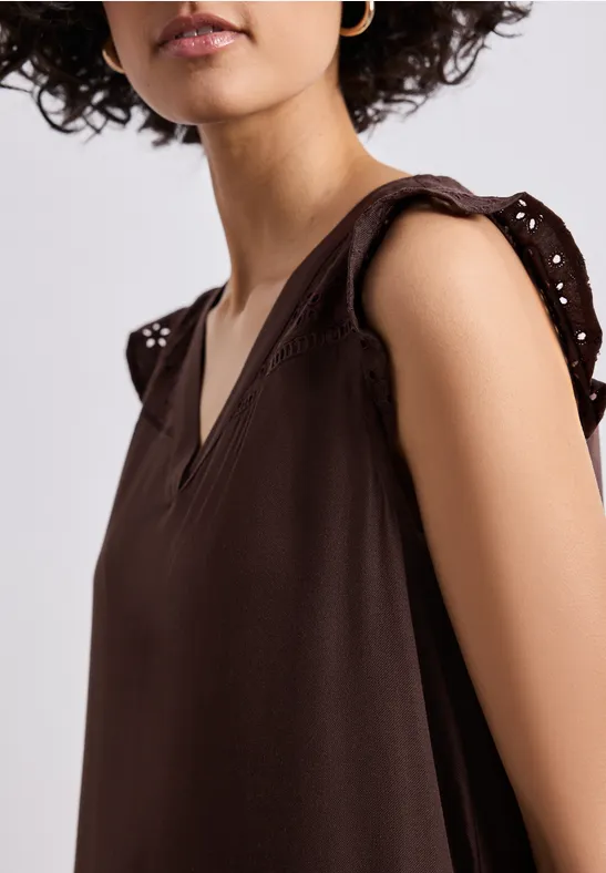 Femme portant un haut marron sans manches à encolure V et manches ajourées décoratives.