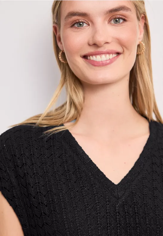 Eine Frau mit langen blonden Haaren trägt einen schwarzen V-Ausschnitt-Pullover.