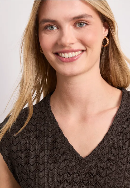 Femme aux cheveux blonds, boucle d’oreilles dorées, portant un haut noir texturé à col en V.