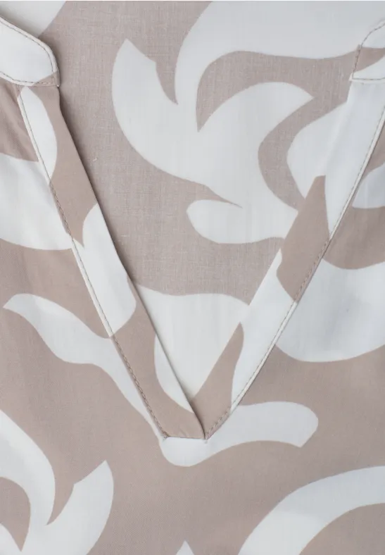 V-halsopname van beige stof met witte, abstracte bladmotieven.