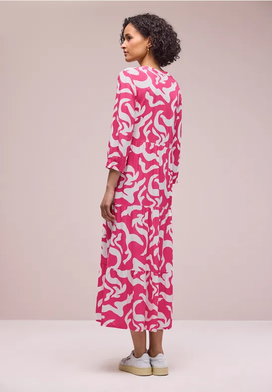 Frau von hinten in einem langen pink-weißen gemusterten Kleid und weißen Schuhen.