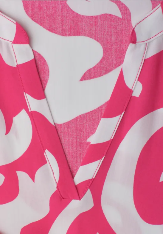 Nahaufnahme eines V-Ausschnitt-Oberteils mit weißem Grund und pinkem, organischem Muster