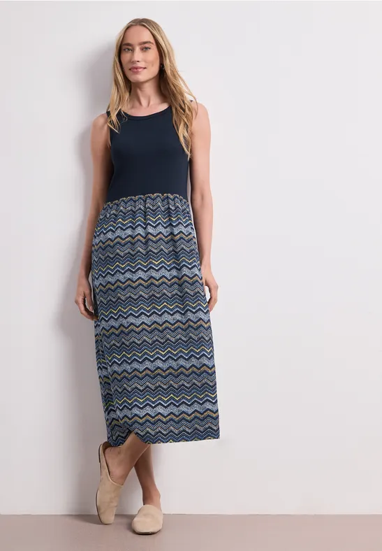 Frau trägt ärmelloses Maxi-Kleid mit dunkelblauem Oberteil und gemustertem, mehrfarbigem Zickzack-Rock.