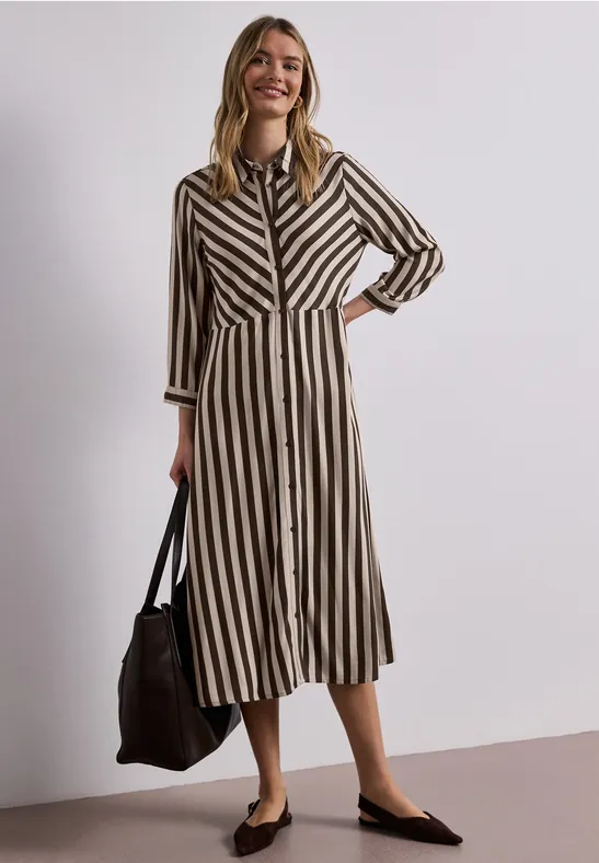 Frau trägt midi Hemdkleid in Schwarz-Beige-Streifen, mit schwarzer Tasche und schwarzen flachen Schuhen.