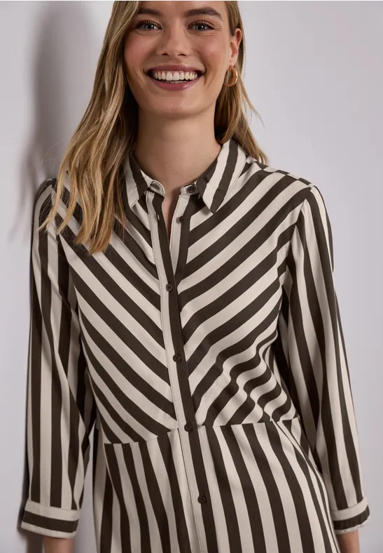 Eine Frau trägt eine Hemdbluse mit diagonalen schwarz-beigen Streifen.