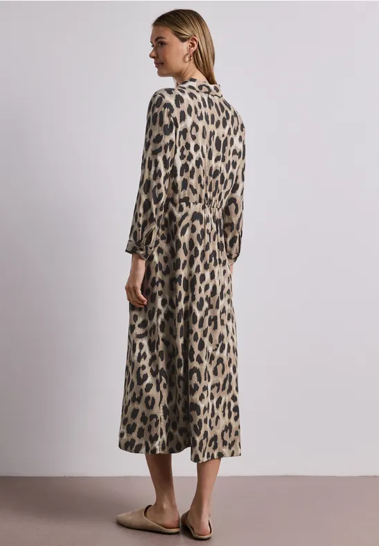 Vrouw in midi-jurk met luipaardprint en driekwartmouwen, zijwaarts staand voor neutrale achtergrond