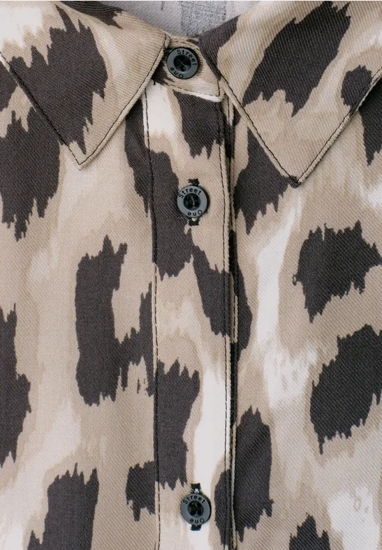 Close-up van een beige-bruin overhemd met dierenprintvlekken en zwarte knopen.