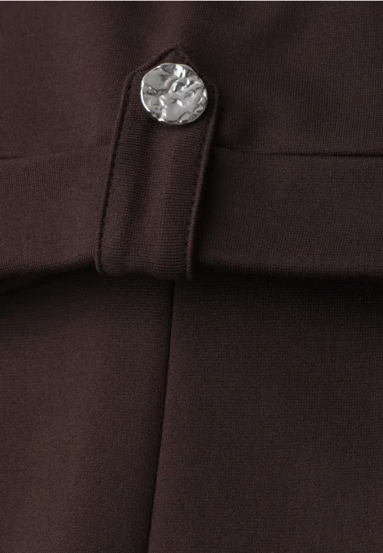 Detailaufnahme eines dunkelbraunen Kleidungsstücks mit silberner, münzförmiger Knopfverzierung und Riegel.