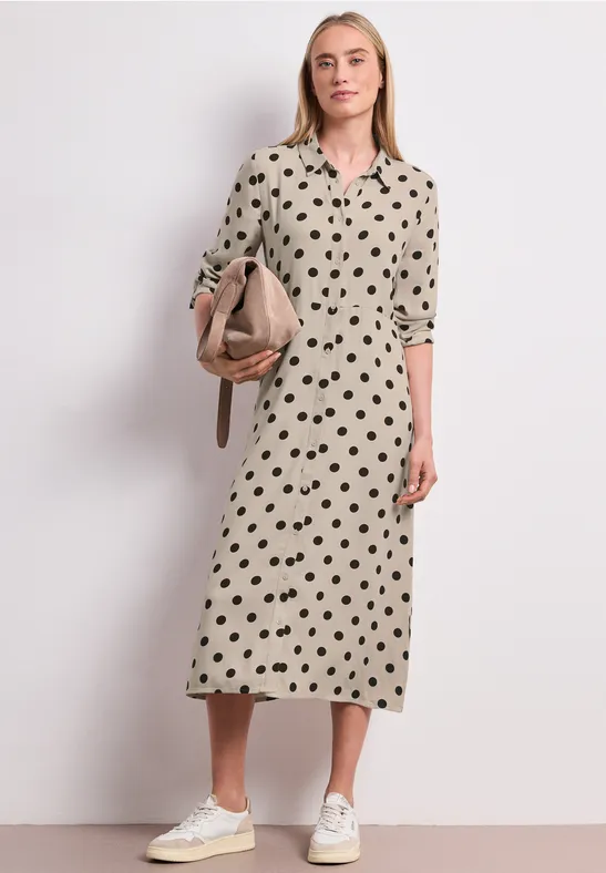 Femme en robe midi beige à motif cœurs noirs, baskets blanches et sac épaule beige.