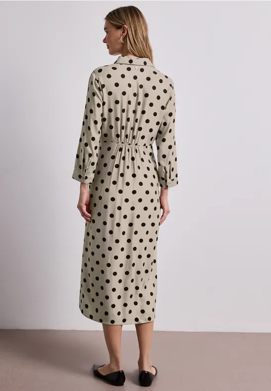 Femme vue de dos portant une robe midi beige à pois noirs, manches 3/4 et chaussures plates