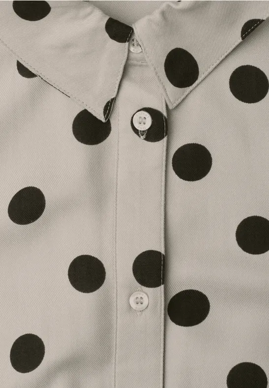 Gros plan d’une chemise crème à pois noirs avec boutons visibles.