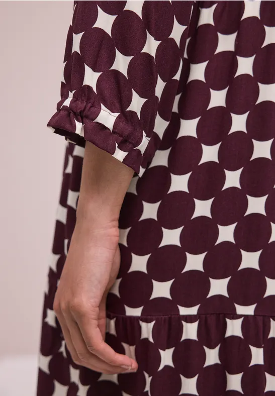 Nahaufnahme einer Hand und eines Arms in lockerem Kleid mit weißen Kreisen auf dunkelrotem Stoff.