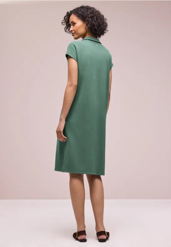 Eine Frau von hinten trägt ein grünes, knielanges Polo-Kleid mit kurzen Ärmeln und schwarzen Sandalen.