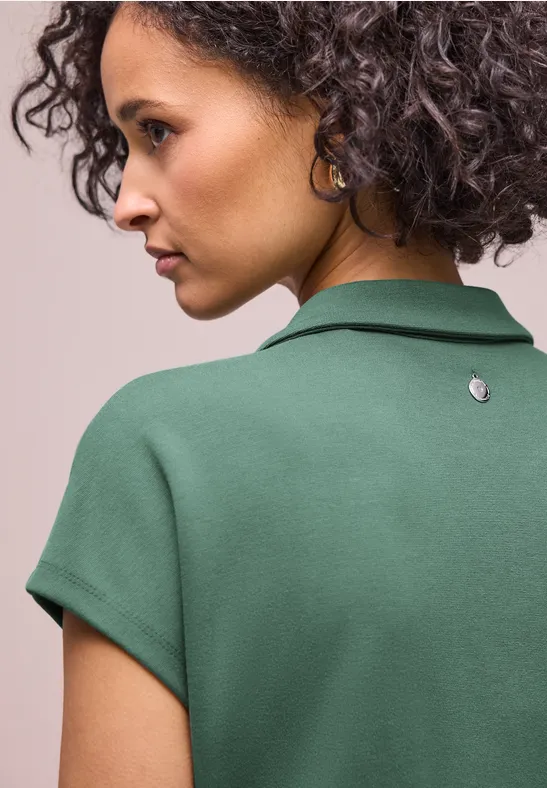 Rückansicht einer Person mit lockigem Haar, die ein grünes Polohemd trägt.