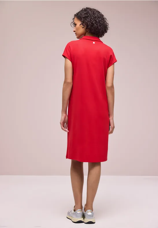 Frau von hinten in rotem Polokleid und Sneakern vor neutralem Hintergrund.