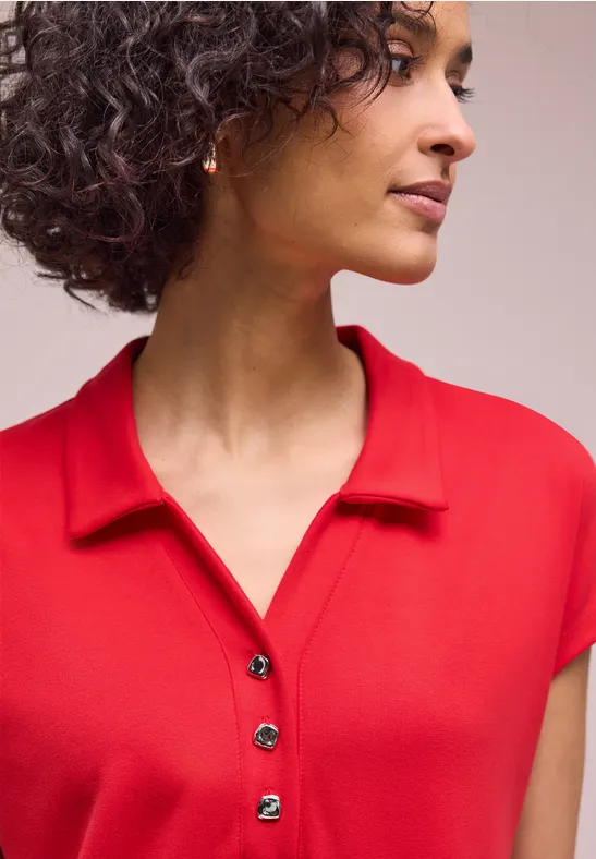 Eine Person mit lockigem Haar trägt ein rotes Poloshirt.