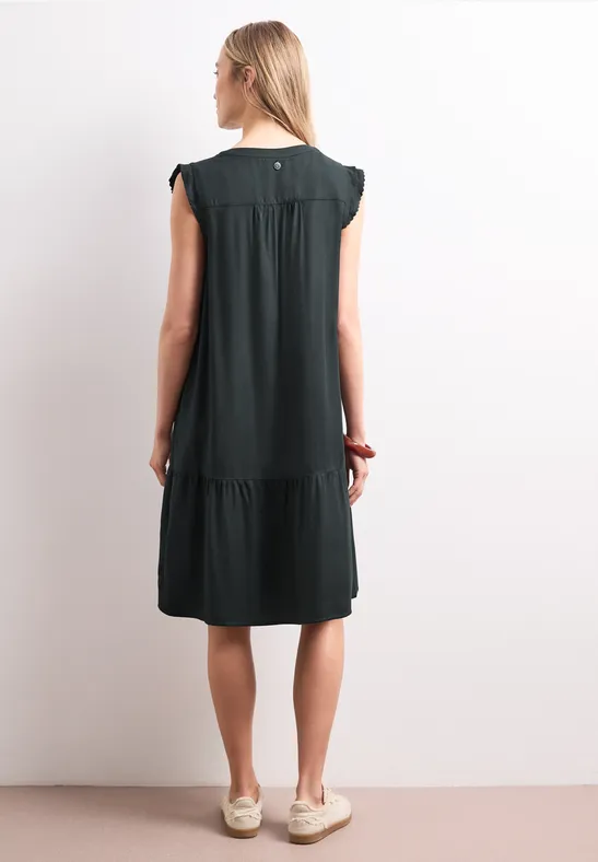 Femme de dos portant une robe noire courte à manches courtes et volants.