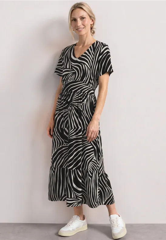Femme en robe midi zébrée noir et blanc avec baskets blanches devant un mur clair.