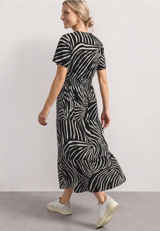 Femme portant une robe midi à motif zèbre noir et blanc, manches courtes, baskets blanches.