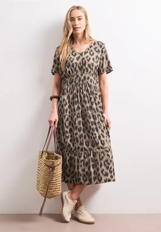 Frau in modischem Midikleid mit Leopardenmuster, trägt Korbtasche und bequeme Sneaker.