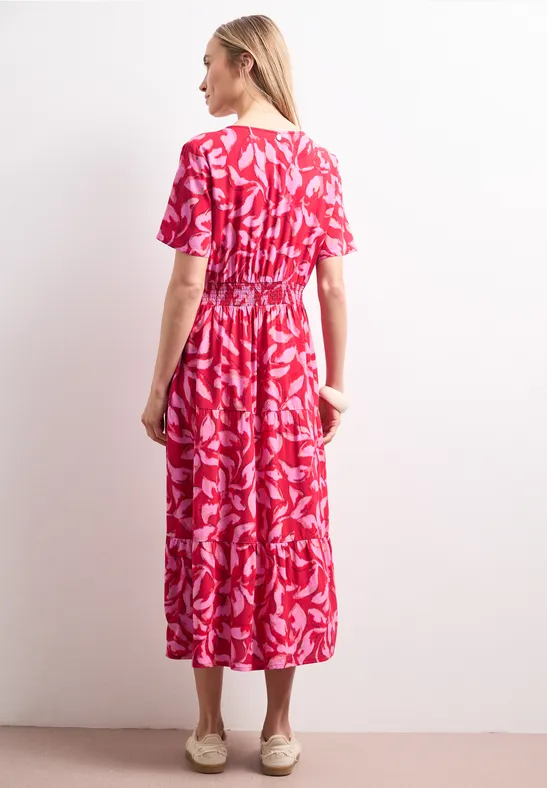 Femme vue de dos portant une robe mi-longue évasée à motifs feuilles rouges et blanches.