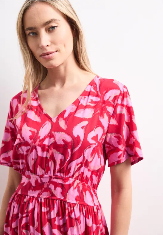 Femme en robe courte rose et rouge à encolure en V, motif floral, taille cintrée.