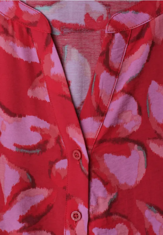 Rood gebreid kledingstuk met roze-lila abstracte patronen, V-hals met knopen.