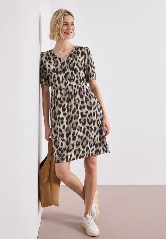Frau trägt kurzärmliges Leopardenkleid mit weißen Sneakers und brauner Tasche.