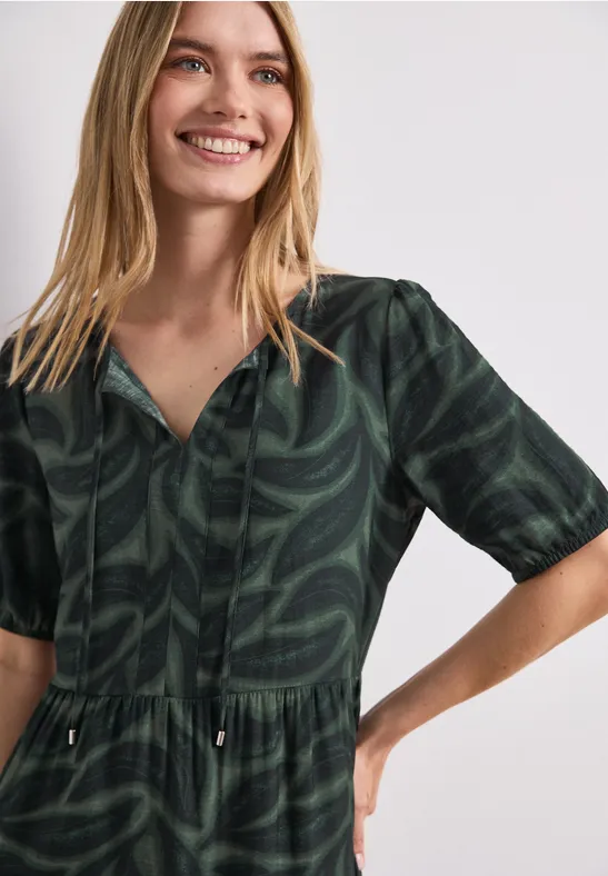 Vrouw in donkergroen midi-jurk met bladmotief, halflange mouwen en V-hals.