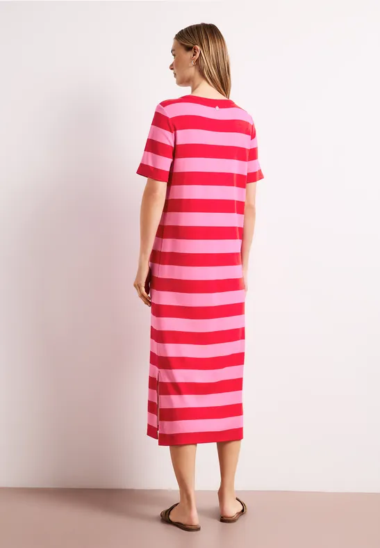 Een vrouw staat zijwaarts in een midi-jurk met rode en roze strepen.