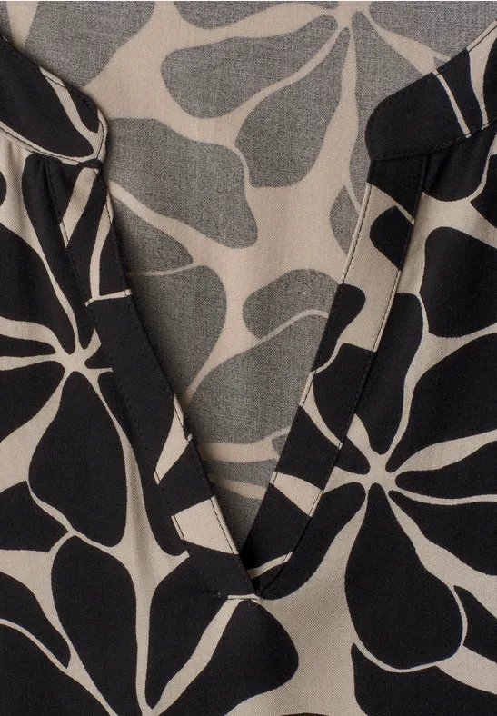 Beige stof met zwart abstract bloemenpatroon en V-hals, close-up.