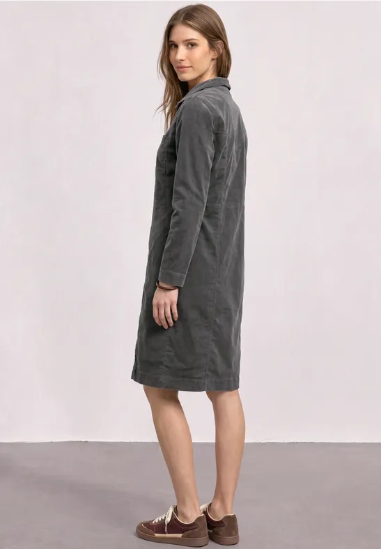 Vrouw in zijaanzicht draagt een grijze corduroy midi-jurk voor een neutrale achtergrond.