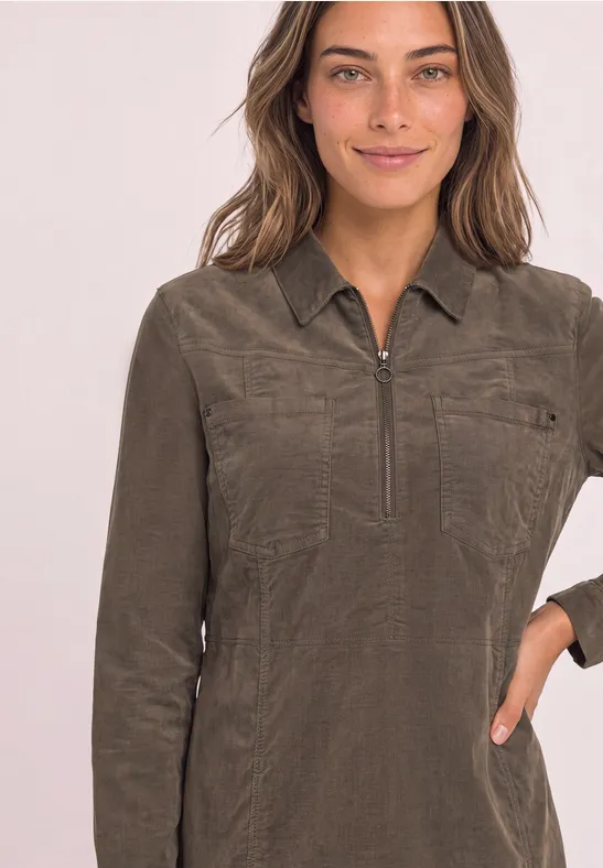 Vrouw draagt kaki shirt met lange mouwen, rits, kraag en borstzakken.