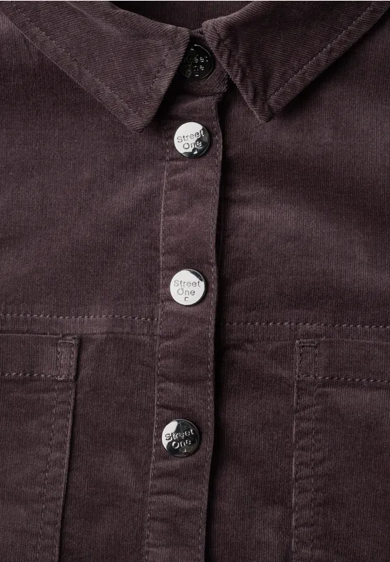 Nahaufnahme einer dunkelbraunen Cordjacke mit silbernen Metallknöpfen und Brusttaschen.