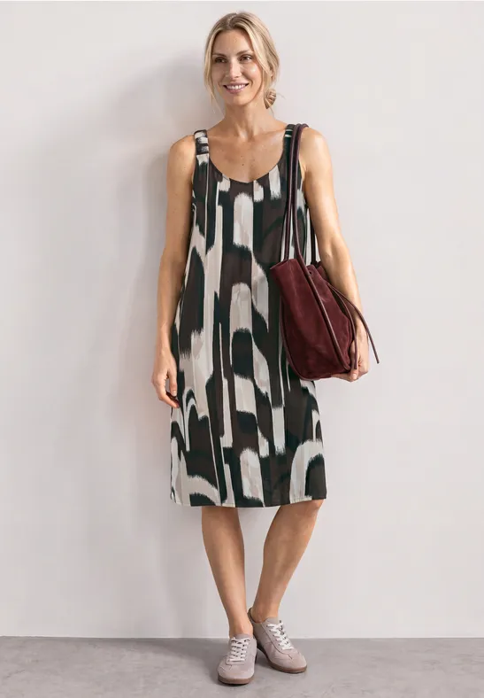 Femme en robe midi sans manches à motifs noir et blanc, portant un sac à bandoulière rouge.