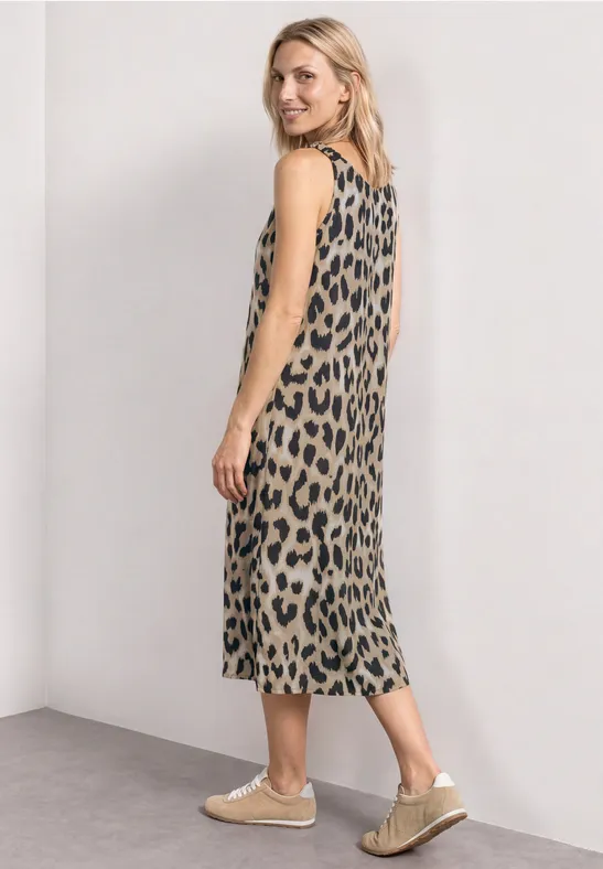 Frau in ärmellosem Midikleid mit Leopardenmuster, seitlich stehend, vor neutralem Hintergrund.