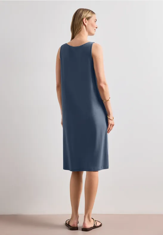 Frau in ärmellosem, knielangem, marineblauem Kleid vor neutralem Hintergrund.