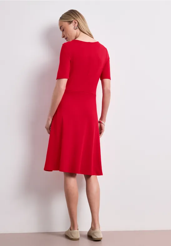 Eine Frau in einem roten, knielangen Kleid mit halblangen Ärmeln, seitliche Rückansicht.
