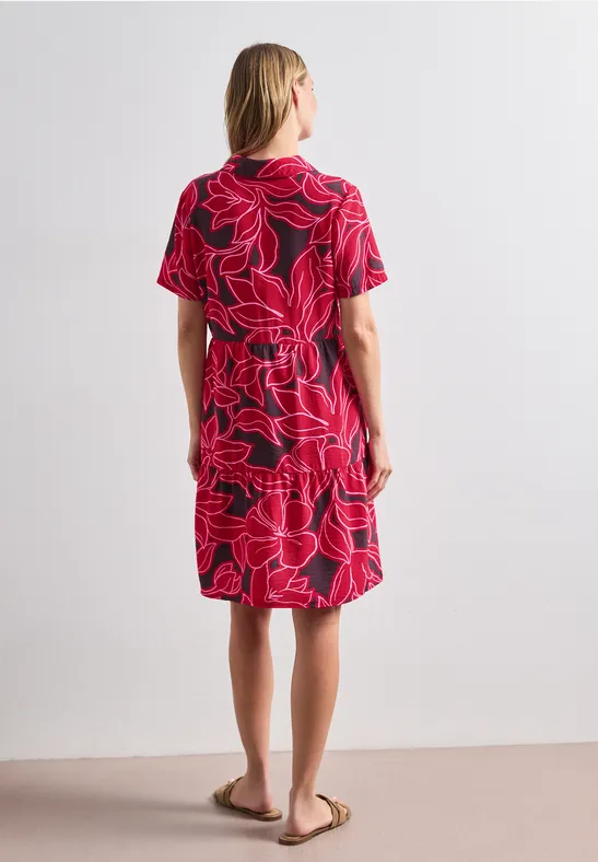 Femme vue de dos portant une robe rouge mi-longue avec un motif linéaire noir abstrait.